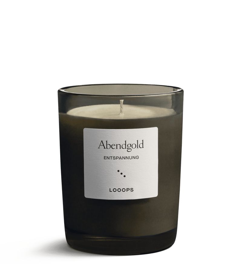 Duftkerze in Glasbehälter. Aufkleber mit "Abendgold", "Entspannung" und "Looops". Schwarzes Glas, weiße Kerze.