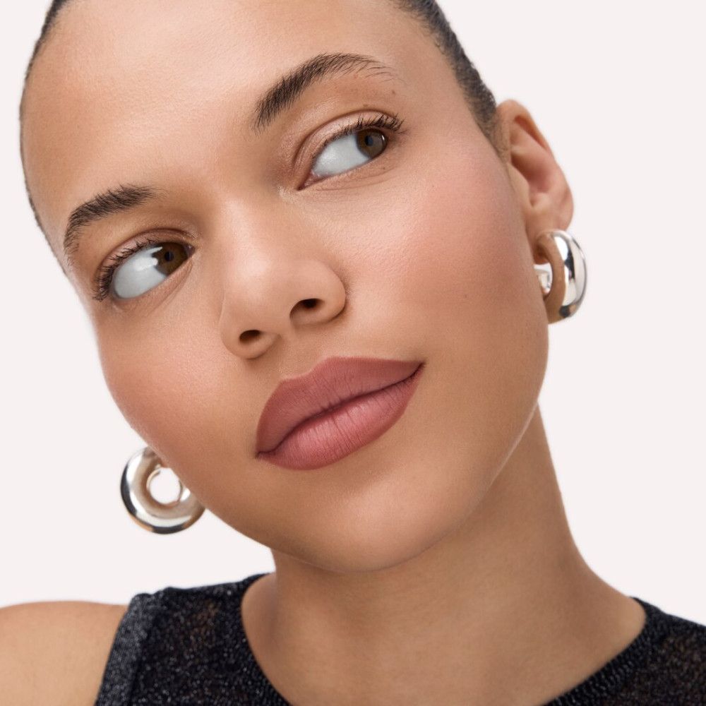 Porträt einer Frau mit geschminkten Lippen. Die Lippen sind mit einem braunen Farbton gefüllt. Die Frau trägt silberne Ohrringe.