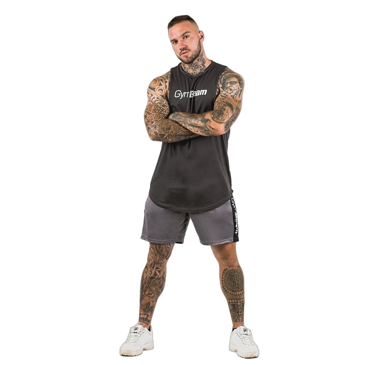 Mann in grauen GymBeam Shorts und schwarzem Tanktop, stehend mit verschränkten Armen.