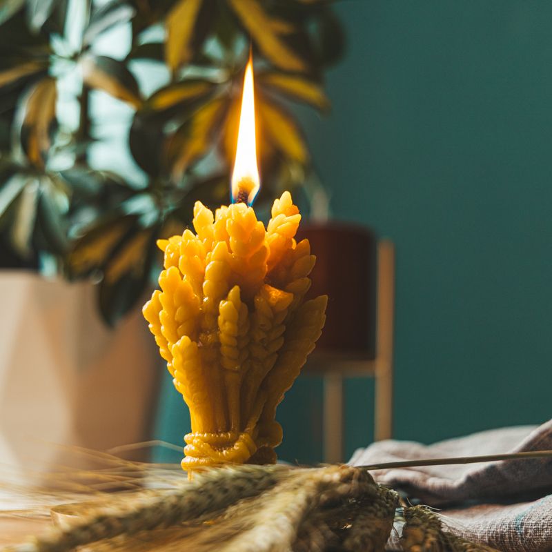 Brennende gelbe Wachskerze in Form eines Weizenbündels. Flamme sichtbar, mit Ähren.