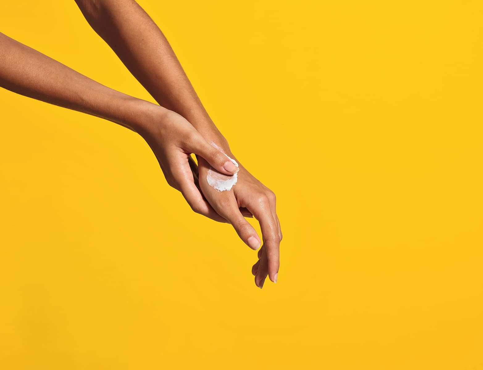 Hände mit Creme auf gelbem Hintergrund. Creme auf einer Hand. Hautpflege.
