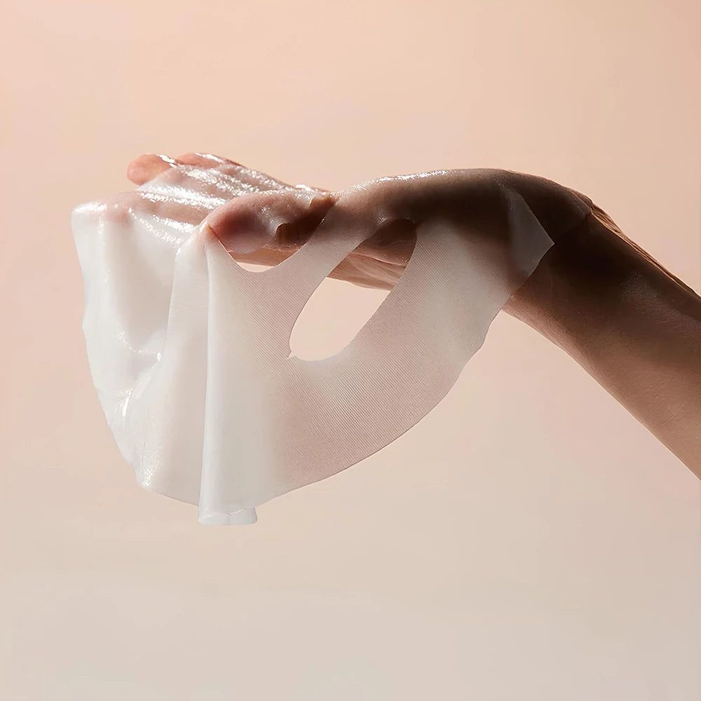 Eine Hand hält eine weiße, feuchte Gesichtsmaske. Die Maske ist transparent und hat Aussparungen für Augen und Mund.