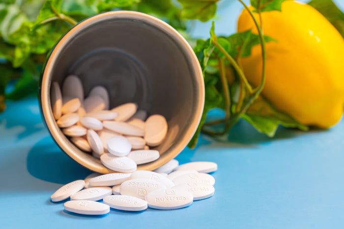 Weiße Tabletten liegen neben einem Becher. Gelbe Zitrone und grüne Blätter im Hintergrund.
