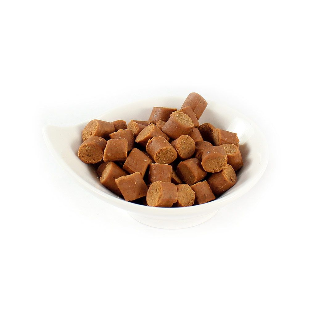Hundesnack in einer weißen Schale. Kleine, zylindrische, braune Stücke. Produktansicht von oben.