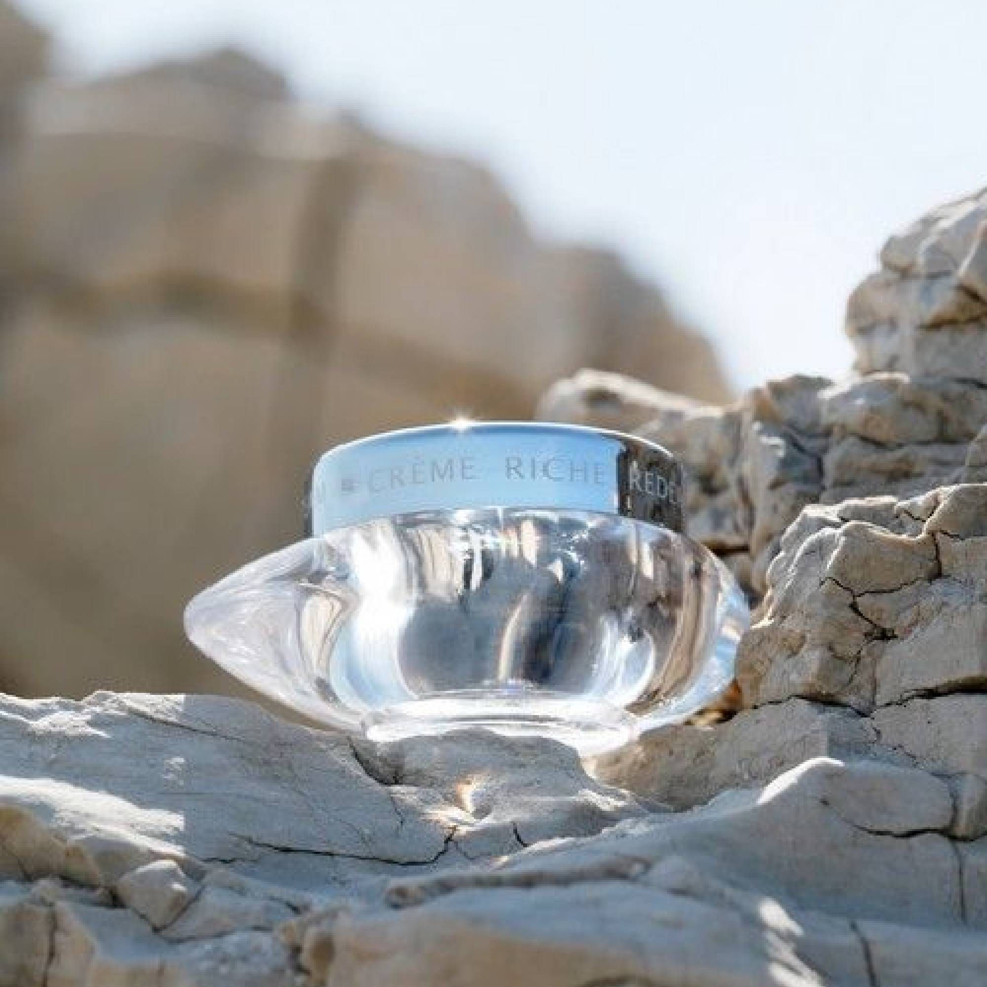 Glasbehälter mit silbernem Deckel auf Felsen. Aufschrift: CREME RICHE REDENSIFIANTE. Produktname: THALGO.