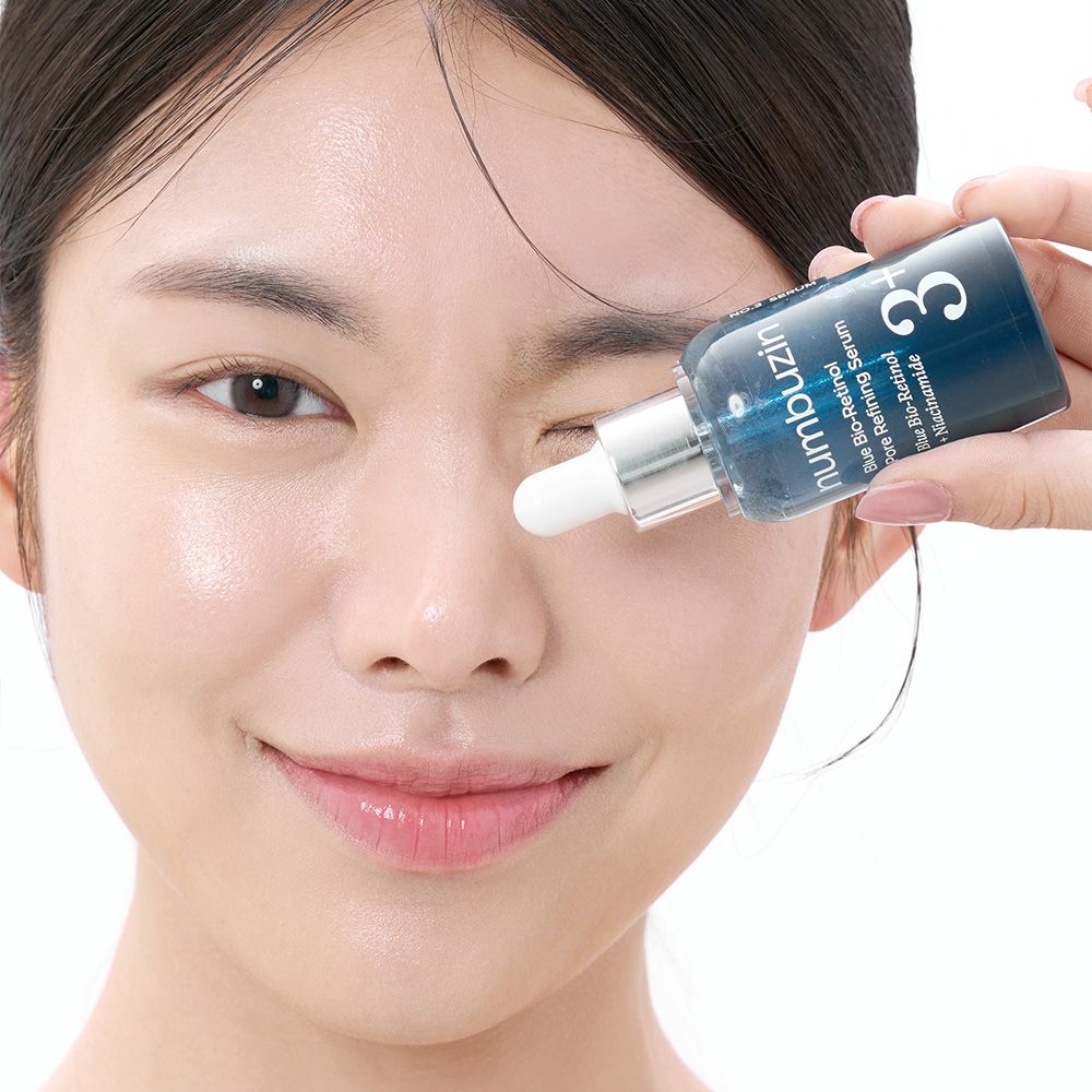 Frau hält Numbuzin No.3 Serum Flasche neben ihrem Auge. Pipette berührt die Haut.