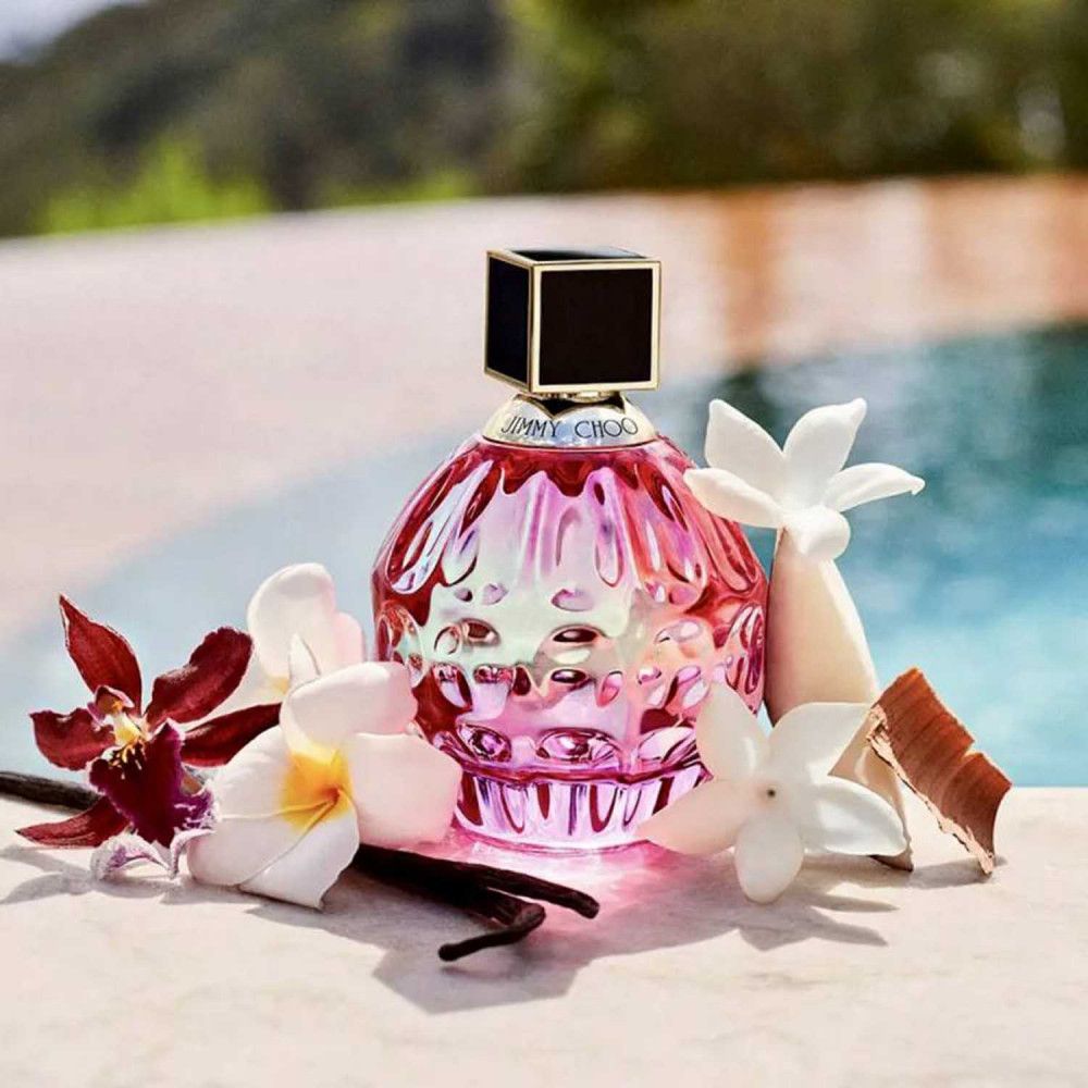 Rosa Flakon mit schwarzem Deckel, umgeben von Blumen und Gewürzen, vor einem Pool.