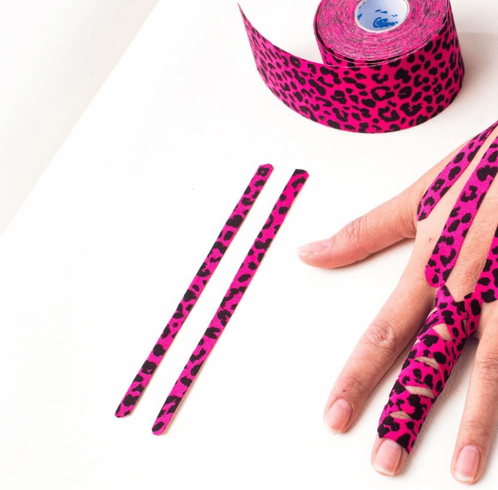 Hand mit pinkfarbenem Kinesiologie-Tape mit Leopardenmuster. Zwei zugeschnittene Streifen liegen daneben.