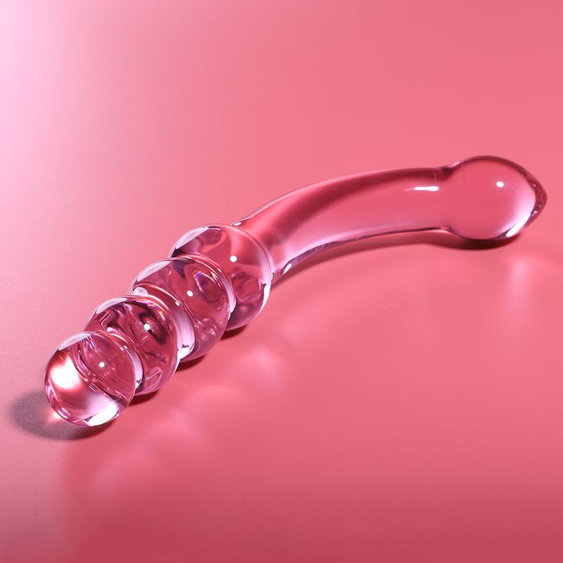 Dildo aus Borosilikatglas. Rosa, transparent. Mit vier kugelförmigen Elementen und gebogener Form. Auf rosa Hintergrund.