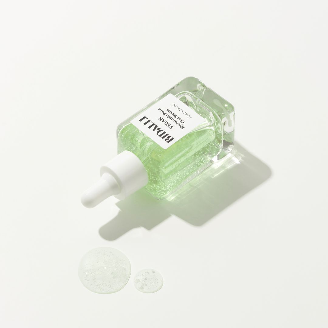 Glasflasche mit grünlicher Flüssigkeit und Pipette. Etikett mit 'Bidalli Vegan Hyaluronic Pure Cica Serum'.