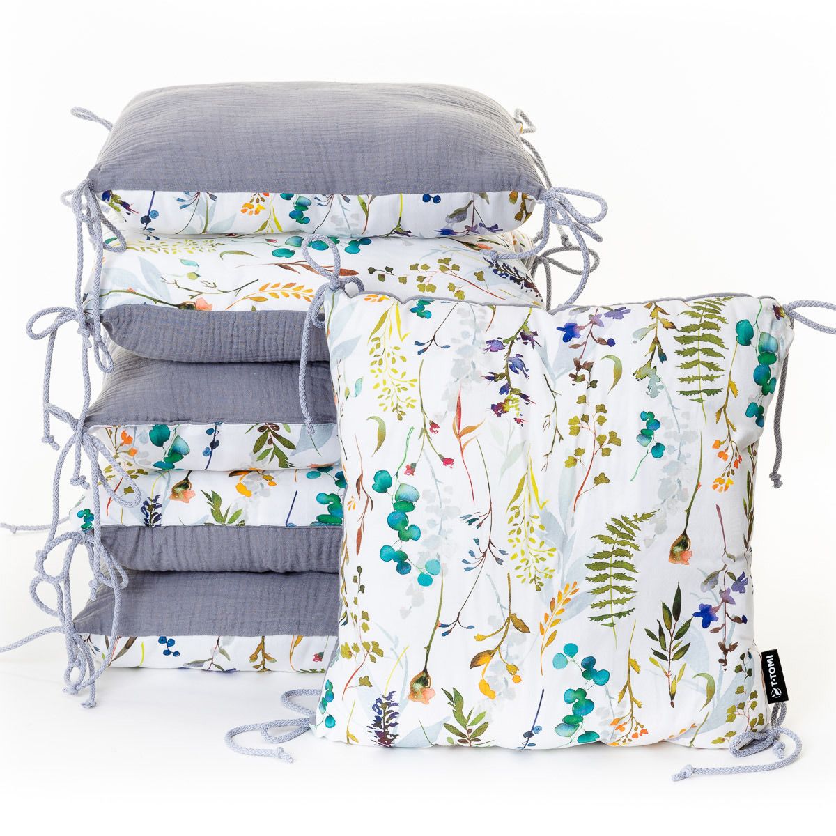 Sechs graue und floral bedruckte Nestchen für ein Babybett, mit Bändern zum Befestigen.