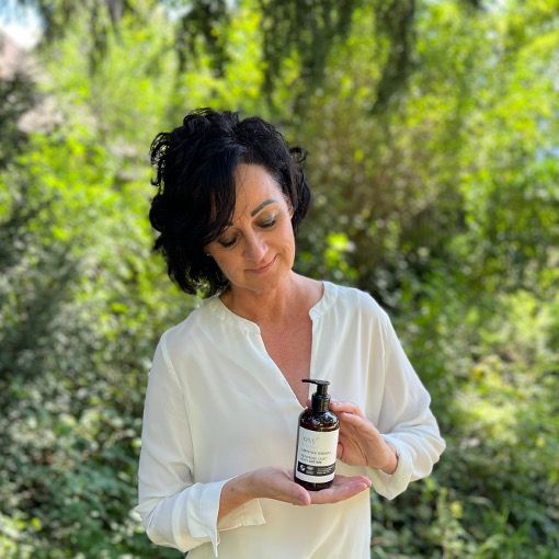 Eine Frau hält eine Flasche Repairing Silky Body Lotion. Aufschrift: Certified Organic, Vegan, Cosmos Organic.