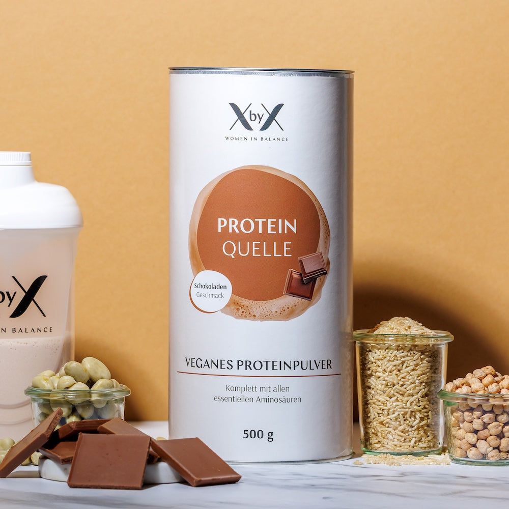 Zylinderdose mit Aufschrift 'Protein Quelle'. Daneben Shaker, Schokoladenstücke, Hülsenfrüchte und Getreidekörner in Gläsern.