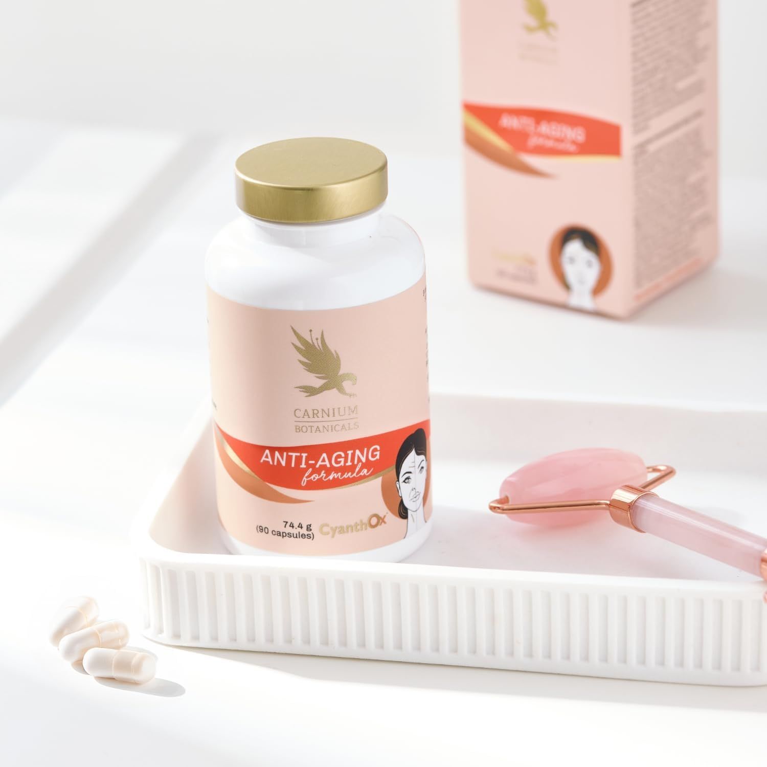 Pillenfläschchen mit goldenem Deckel in weißer Schale. Aufschrift: Anti-Aging formula. Rosenquarz-Roller daneben.