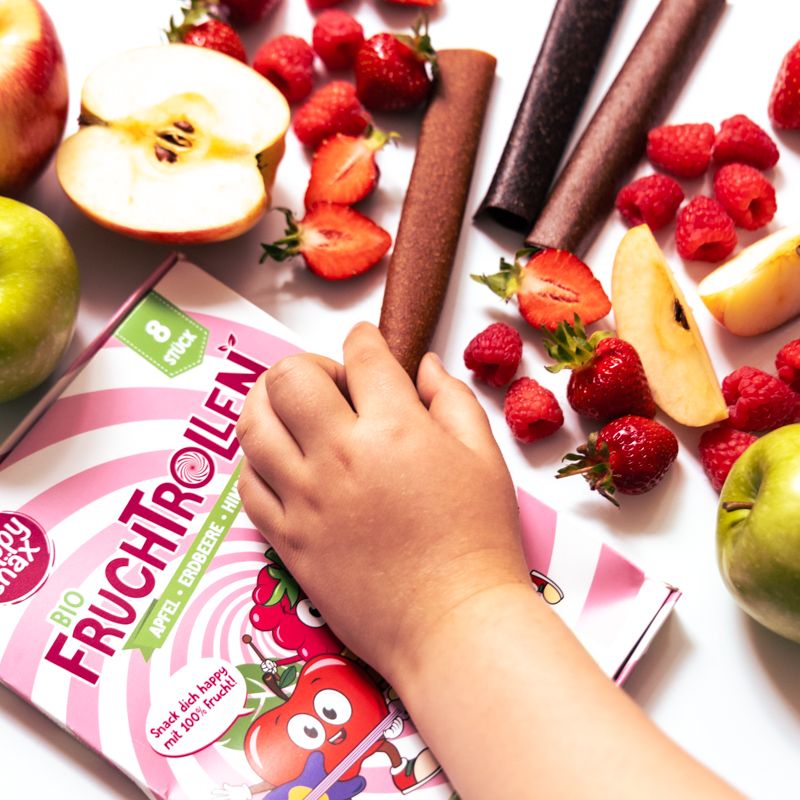 Kind hält eine BIO Fruchtrolle. Verpackung und Früchte liegen daneben.