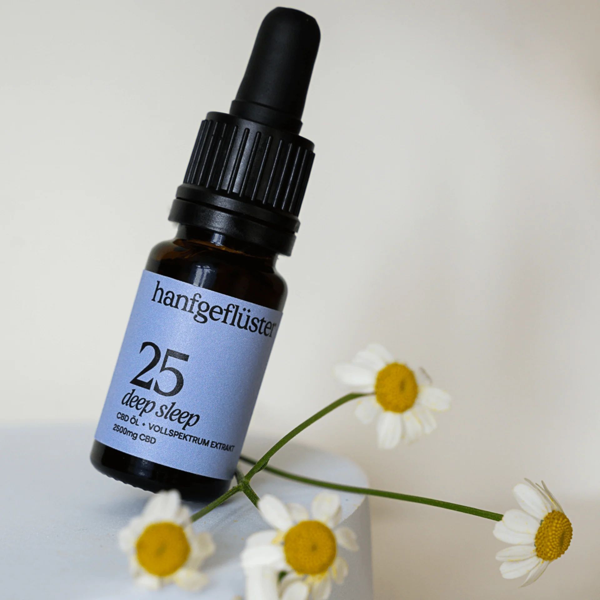 Braune Glasflasche mit schwarzem Tropfer, umgeben von Gänseblümchen. Aufkleber mit "hanfgeflüster", "25 deep sleep".