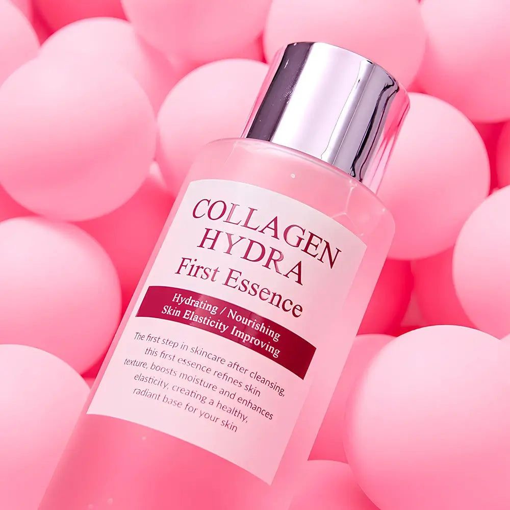 Transparente Flasche mit rosa Flüssigkeit. Aufschrift: Collagen Hydra First Essence. Hintergrund: rosa Kugeln.