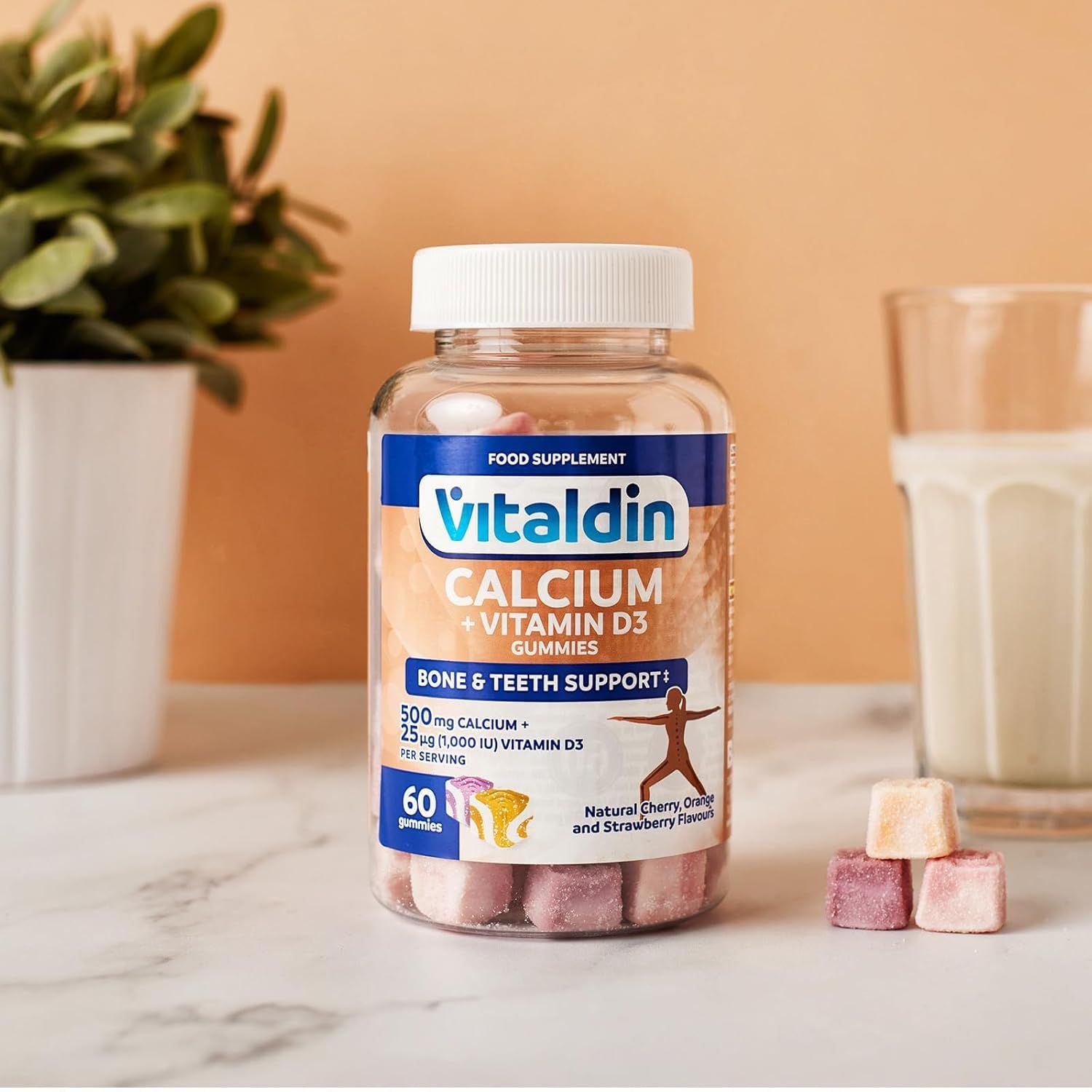 Eine Flasche VITALDIN Calcium + Vitamin D3 Gummies neben einem Glas Milch und drei Gummies. Aufschrift: Knochen- und Zahnunterstützung. Enthält 60 Gummies.