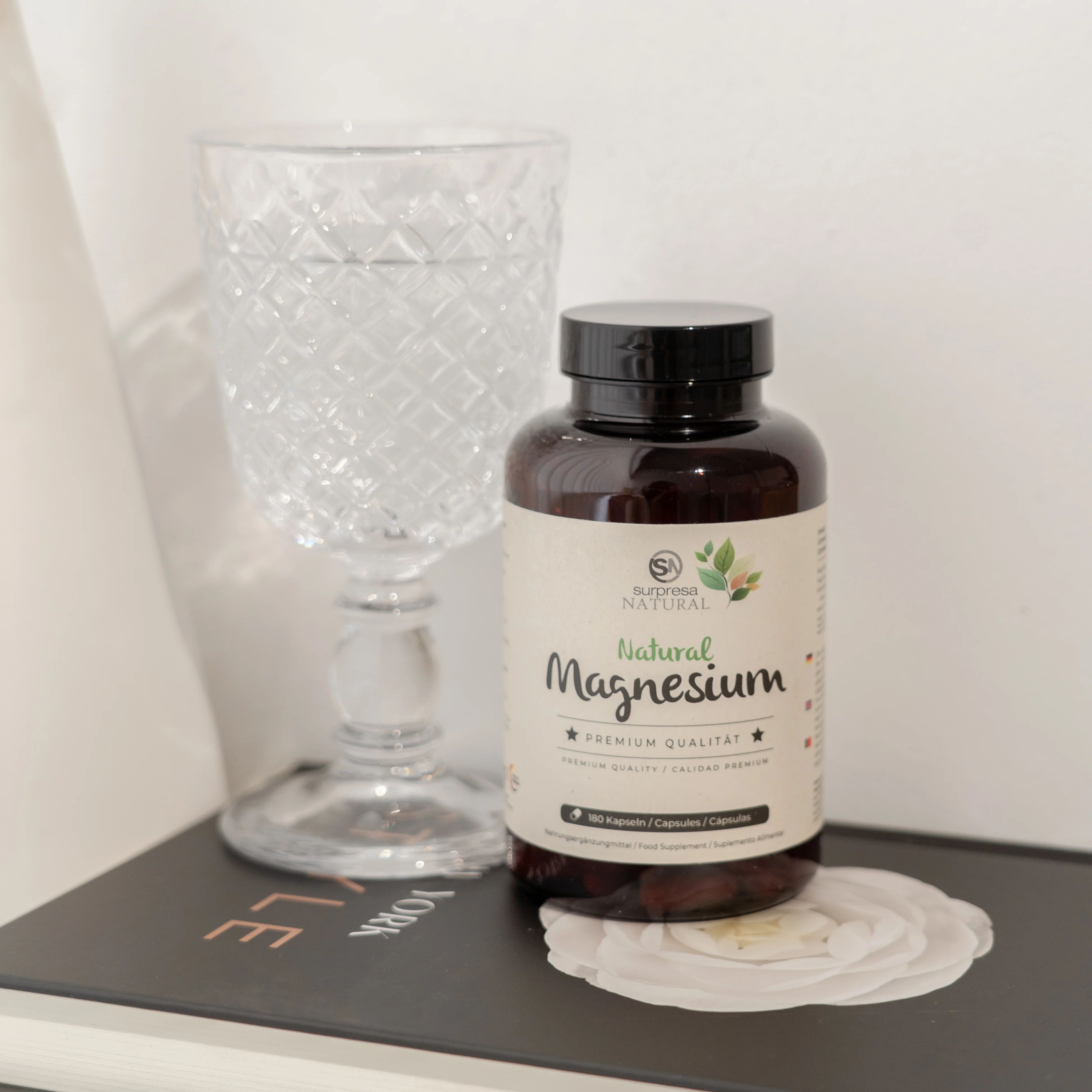 Braune Flasche mit Etikett neben einem Glas Wasser. Aufschrift: Surpresa Natural, Natural Magnesium, Premium Qualität. 180 Kapseln.
