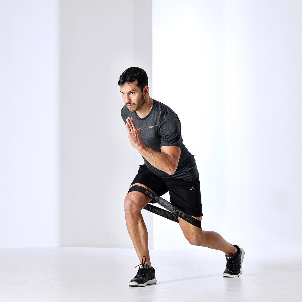 Mann trainiert mit einem schwarzen FLEXVIT Mini-Band um die Beine. Er macht eine Ausfallschrittübung.