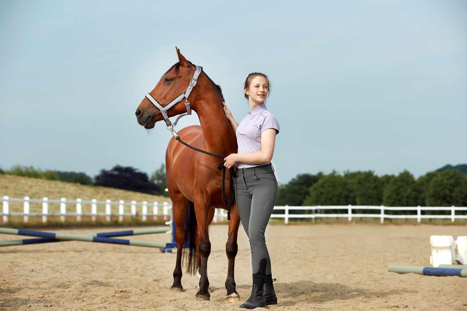 Junge Frau steht neben einem Pferd. Das Pferd trägt ein graues Halfter. Frau hält Zügel.