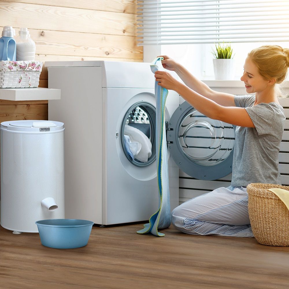 Frau in Waschküche mit Waschmaschine und THOMAS Wäscheschleuder. Blaue Schüssel am Boden.
