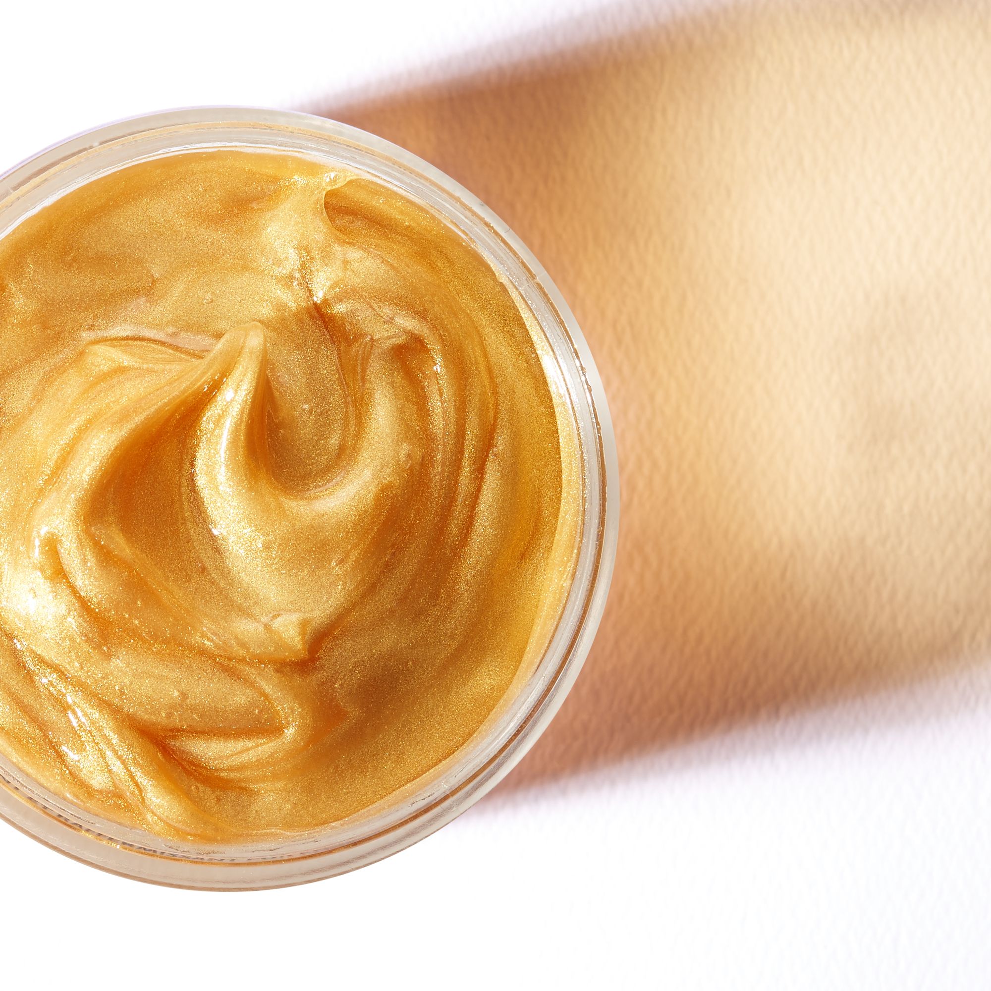 Goldene Gesichtsmaske in einem Glasbehälter. Der Hintergrund ist weiß und beige.