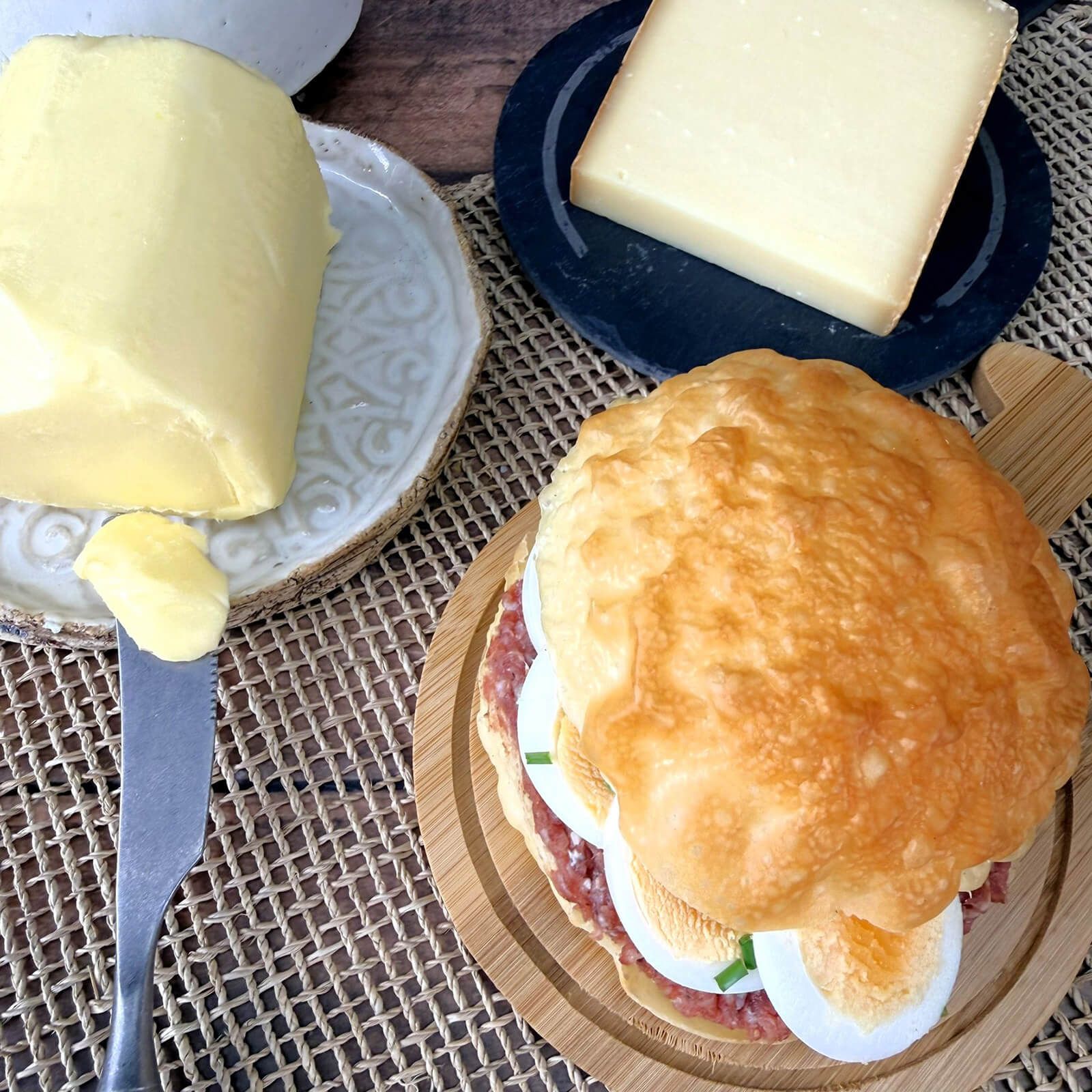 Ein Locawo Dreikäsehoch Brötchen belegt mit Wurst und Ei auf einem Holzbrett.
