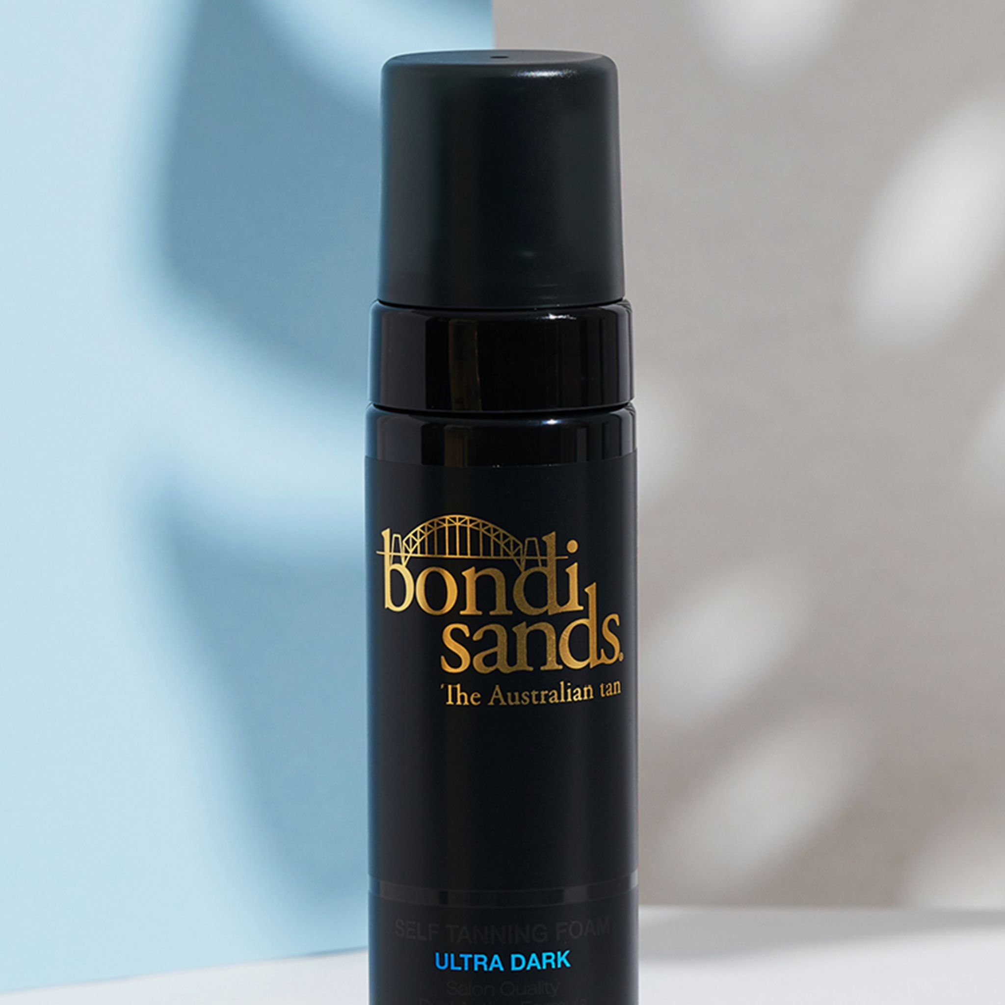 Nahaufnahme einer schwarzen Flasche mit goldenem Logo und schwarzem Sprühkopf. Aufschrift: Bondi Sands, Ultra Dark Selbstbräunungsschaum.