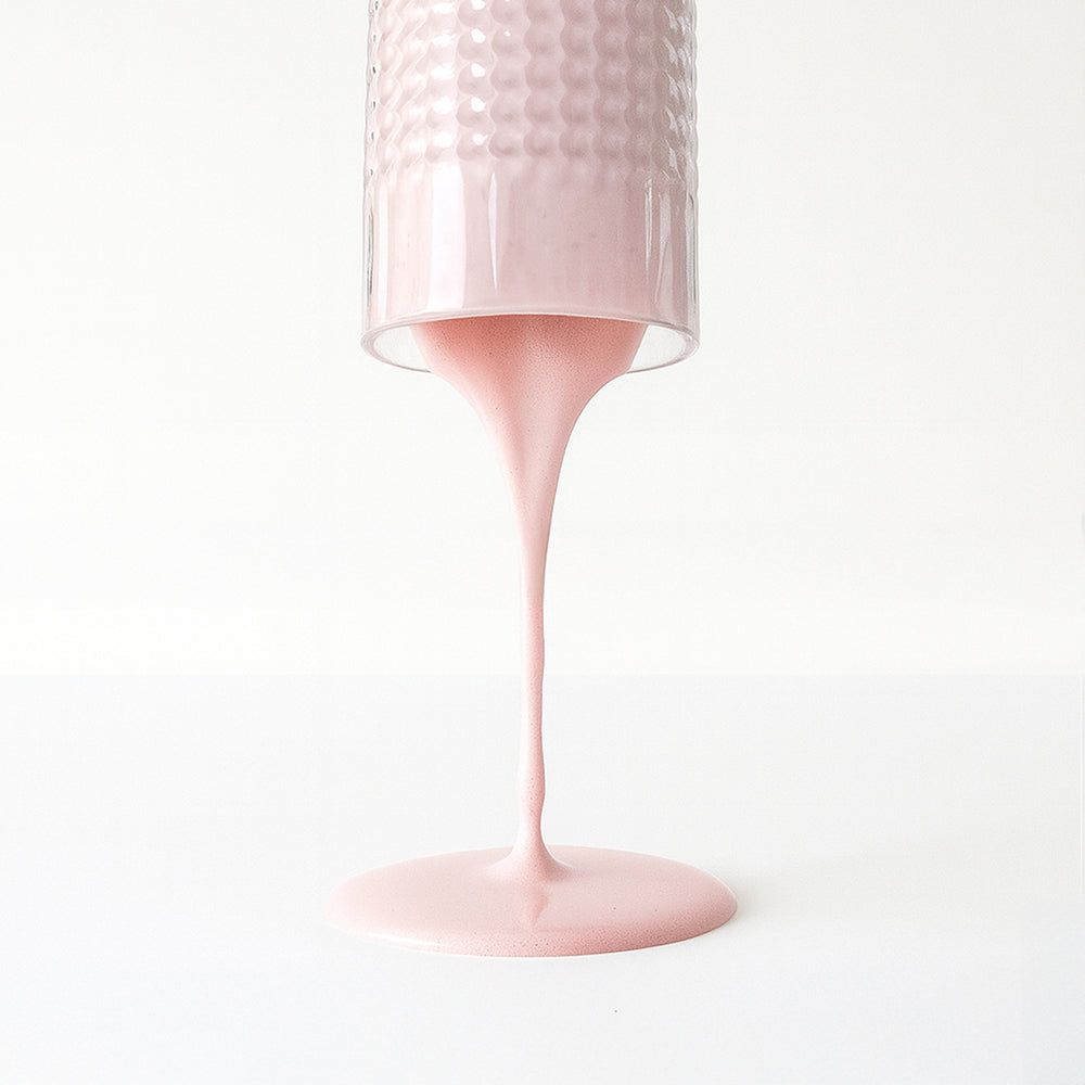 Glas mit rosa Flüssigkeit, die aus dem Glas fließt. Flüssigkeit bildet einen Kreis auf weißem Untergrund.