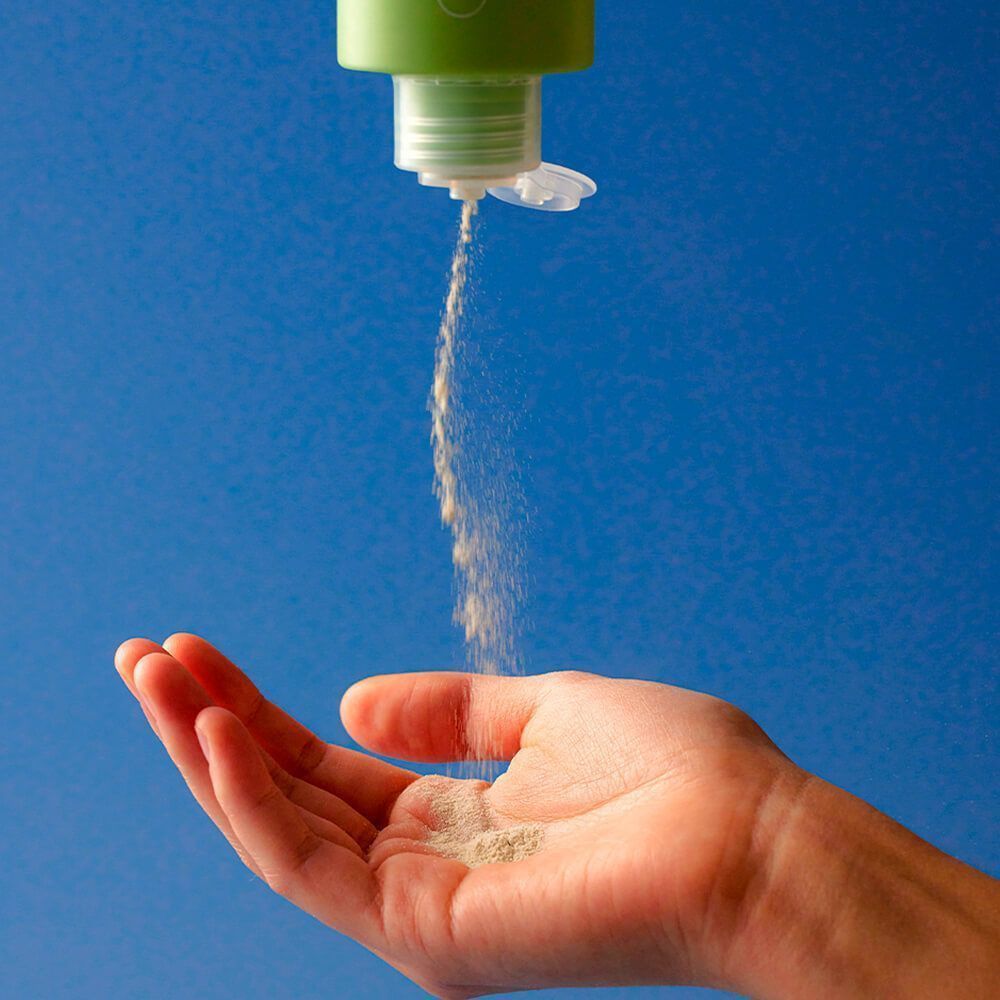 Hand fängt Pulver auf. Pulver kommt aus einer Flasche. Hintergrund: blau.