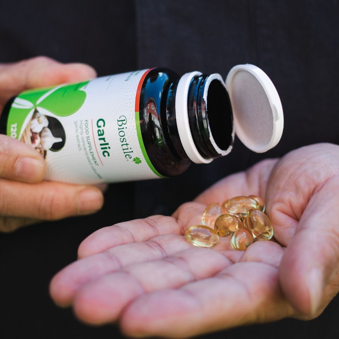 Person hält eine Flasche Biostile Garlic und Kapseln in der Hand. Kapseln sind sichtbar.