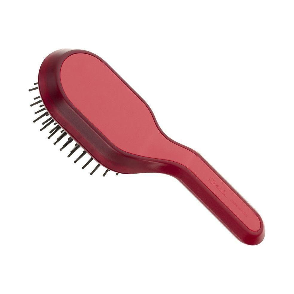 Magentafarbene Haarbürste mit Griff. Rechteckiger Bürstenkopf mit schwarzen Borsten. Abgerundete Form.