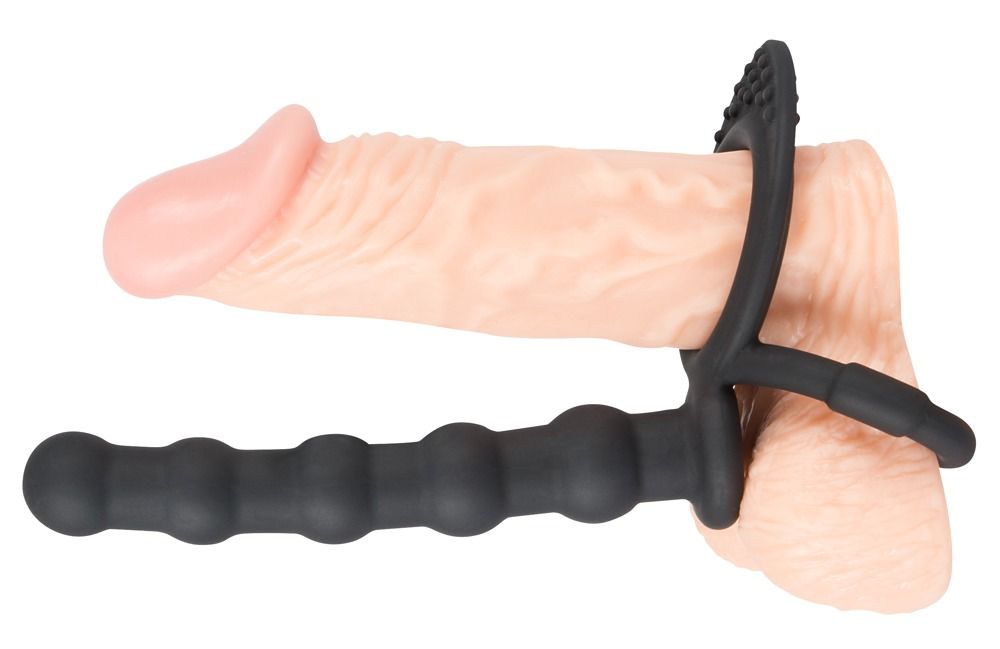 Schwarzer Penis- und Hodenring mit Analdildo, an einem Penis befestigt. Ring mit Noppen, Dildo mit geriffelter Oberfläche.