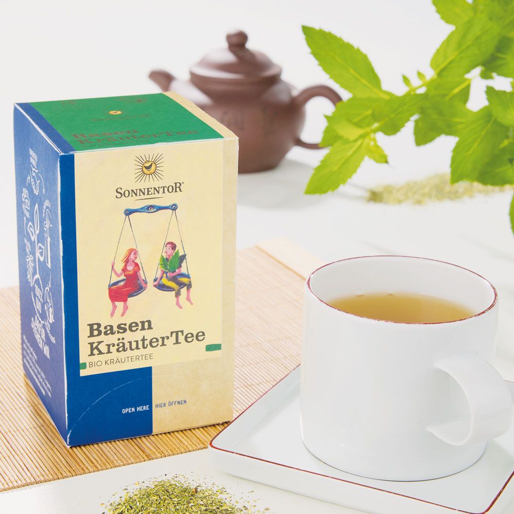 Karton Basen KräuterTee Bio neben Tasse Tee. Logo Sonnentor. Abbildung: Personen auf Waage. Text: Basen KräuterTee, Bio Kräutertee. Zertifizierung.
