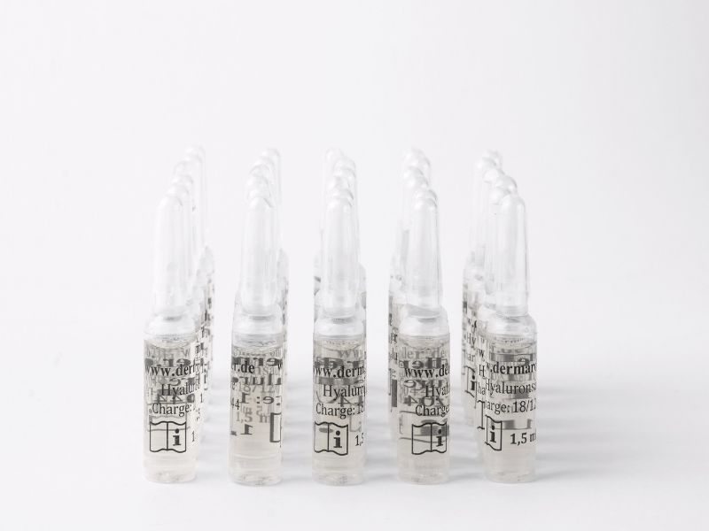Mehrere Glasampullen mit Hyaluronsäure-Serum, weißer Verschluss, weiße Beschriftung.