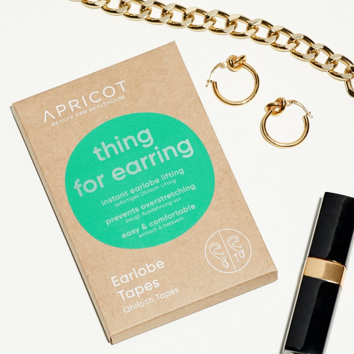 Kartonverpackung mit Produktbeschriftung. Aufschrift: APRICOT, thing for earring, Ohrloch Tapes. Daneben Schmuck und Kosmetik.