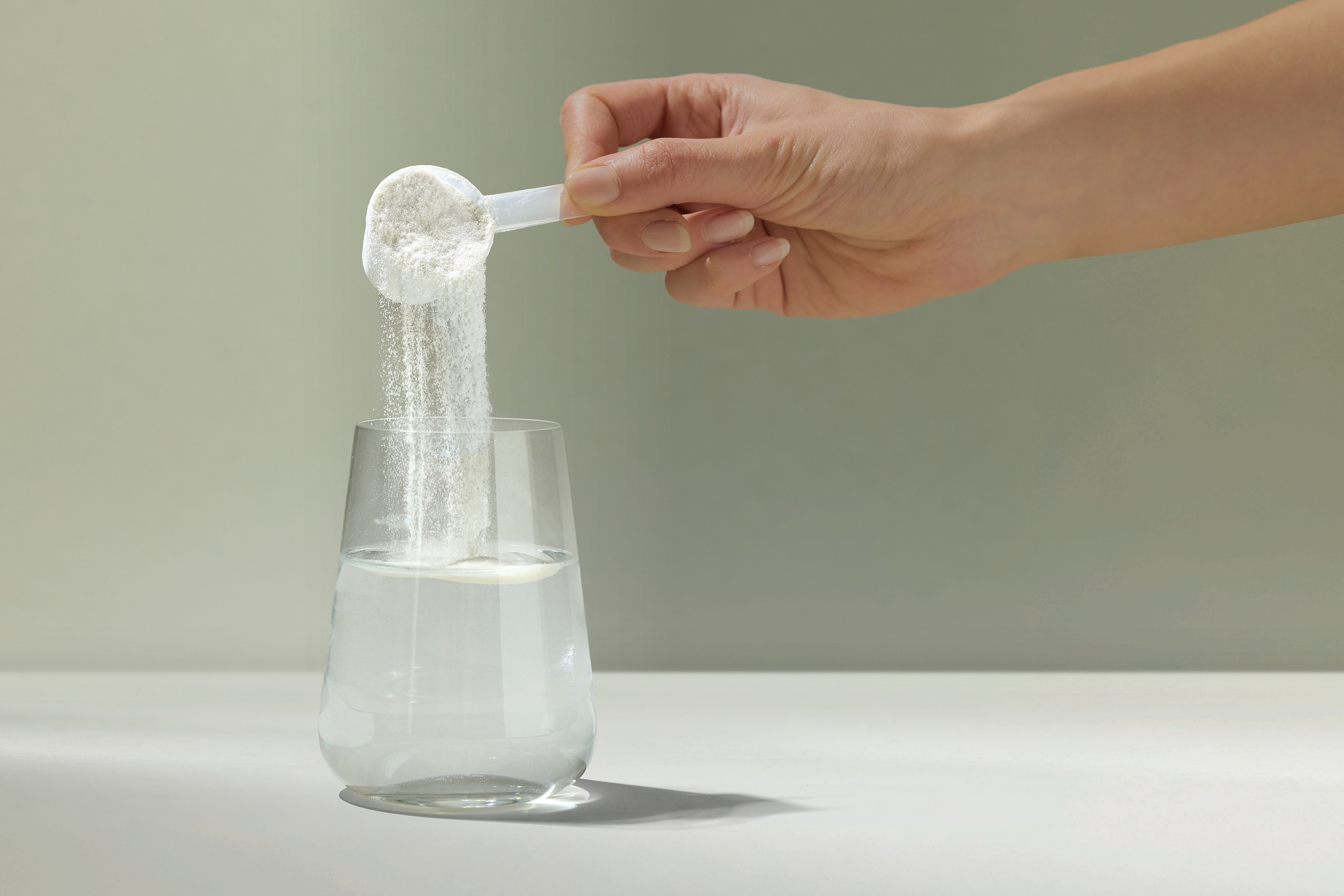 Messlöffel mit VIANOA Kollagen Peptide Pulver wird in ein Glas Wasser geschüttet.