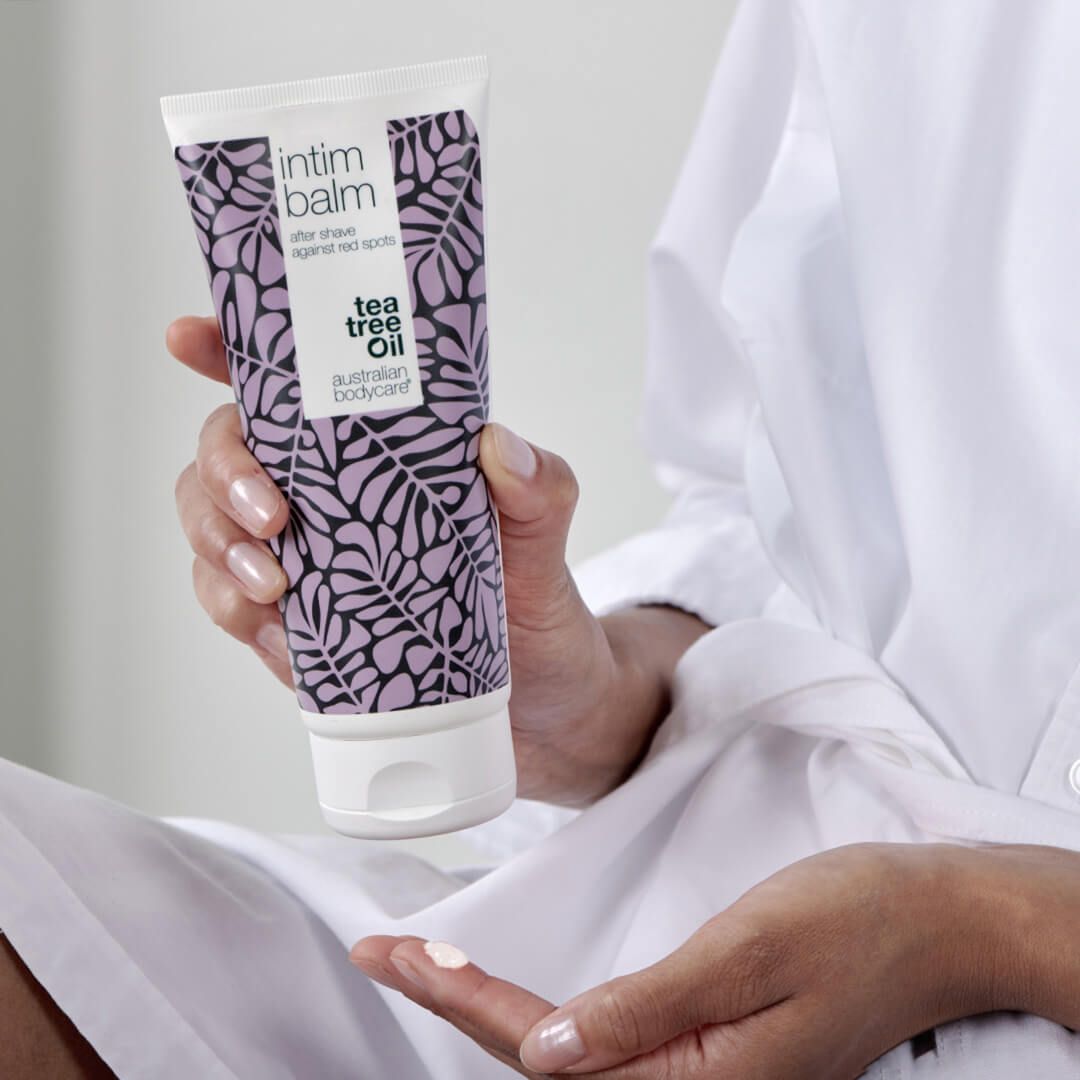 Person hält Tube Intim-Balsam. Weiß-lila Design, Blättermuster. Marke: Australian Bodycare.