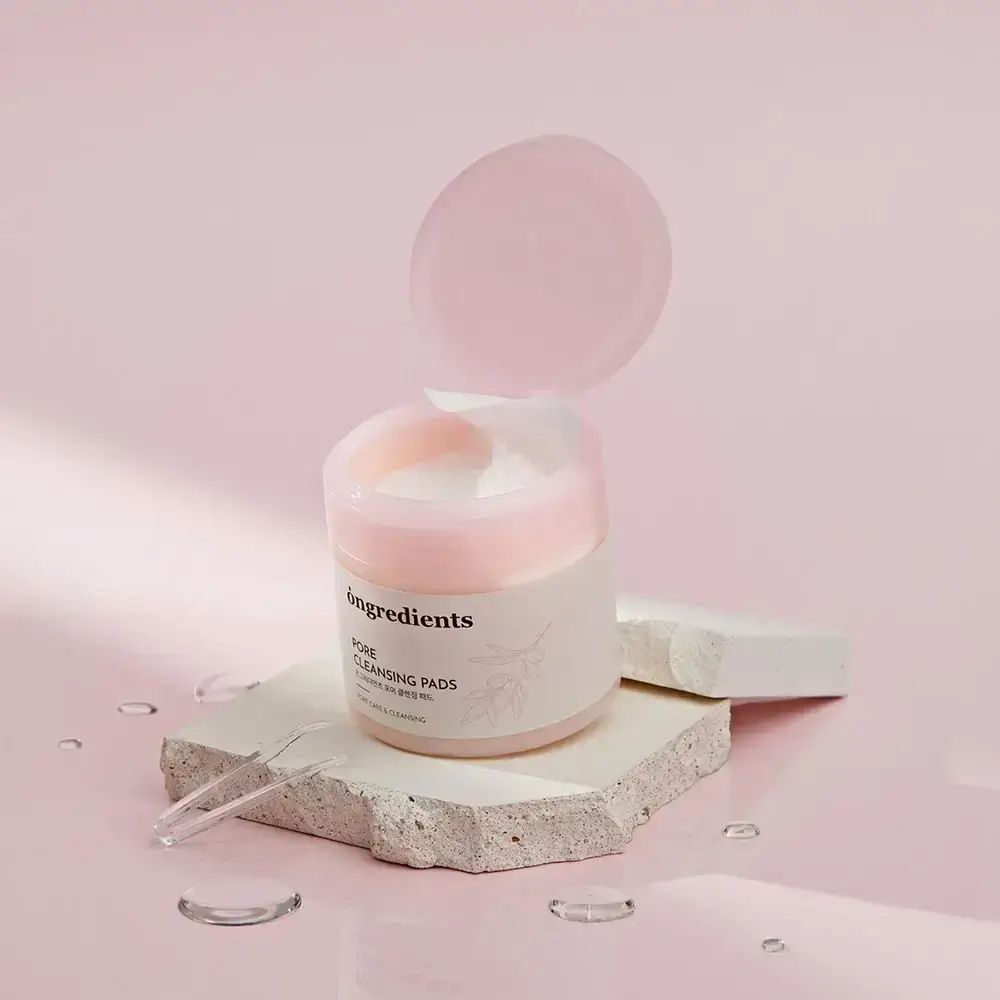 Runde Dose mit rosa Deckel, geöffnet. Aufschrift: Ongredients, Pore Cleansing Pads. Auf Stein platziert.