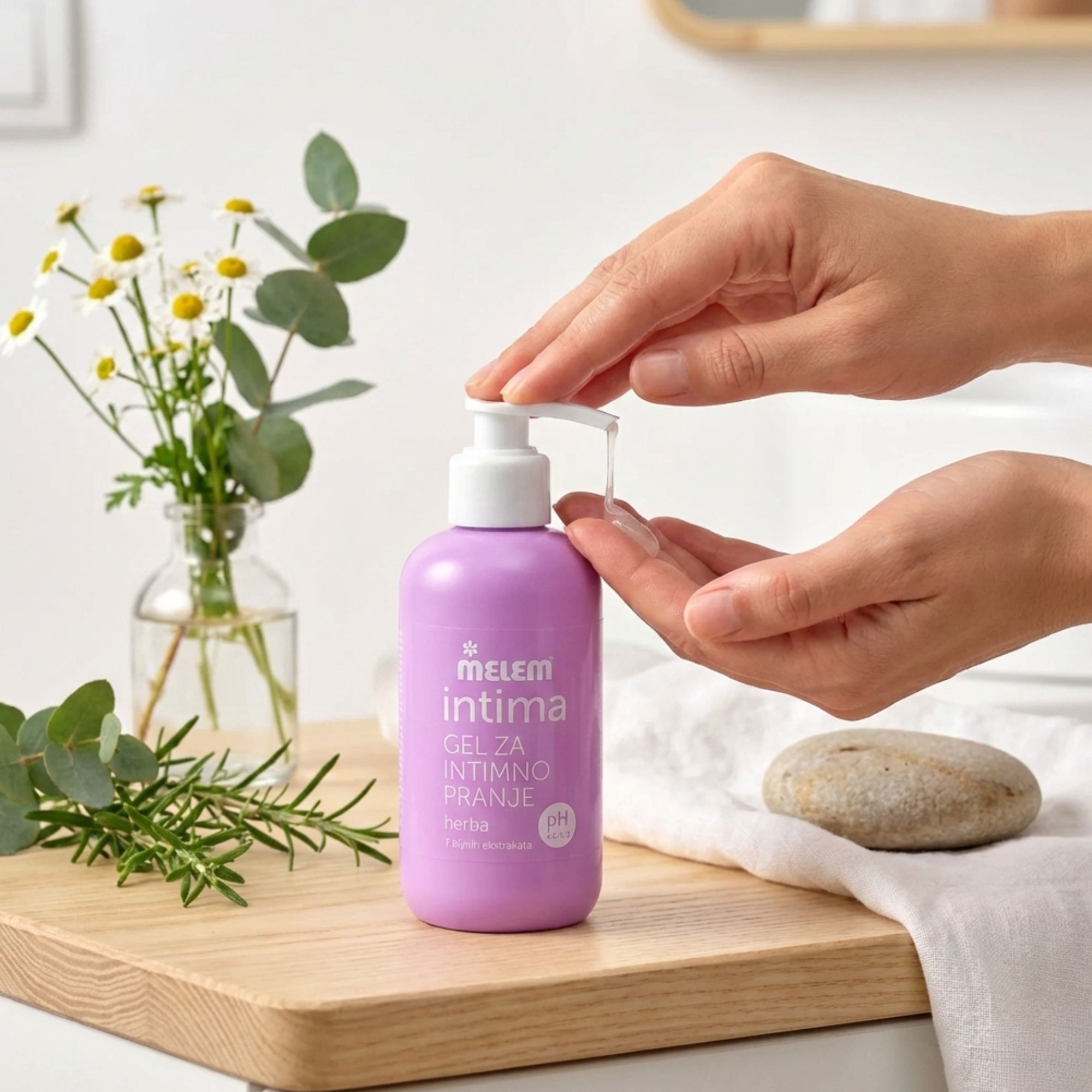 Lila Flasche Intim-Gel mit Pumpe. Hände drücken Gel aus. Daneben Kamille und ein Tuch. Aufschrift: Melem intima, Gel za intimno pranje, herba, pH 4.5-5.0.