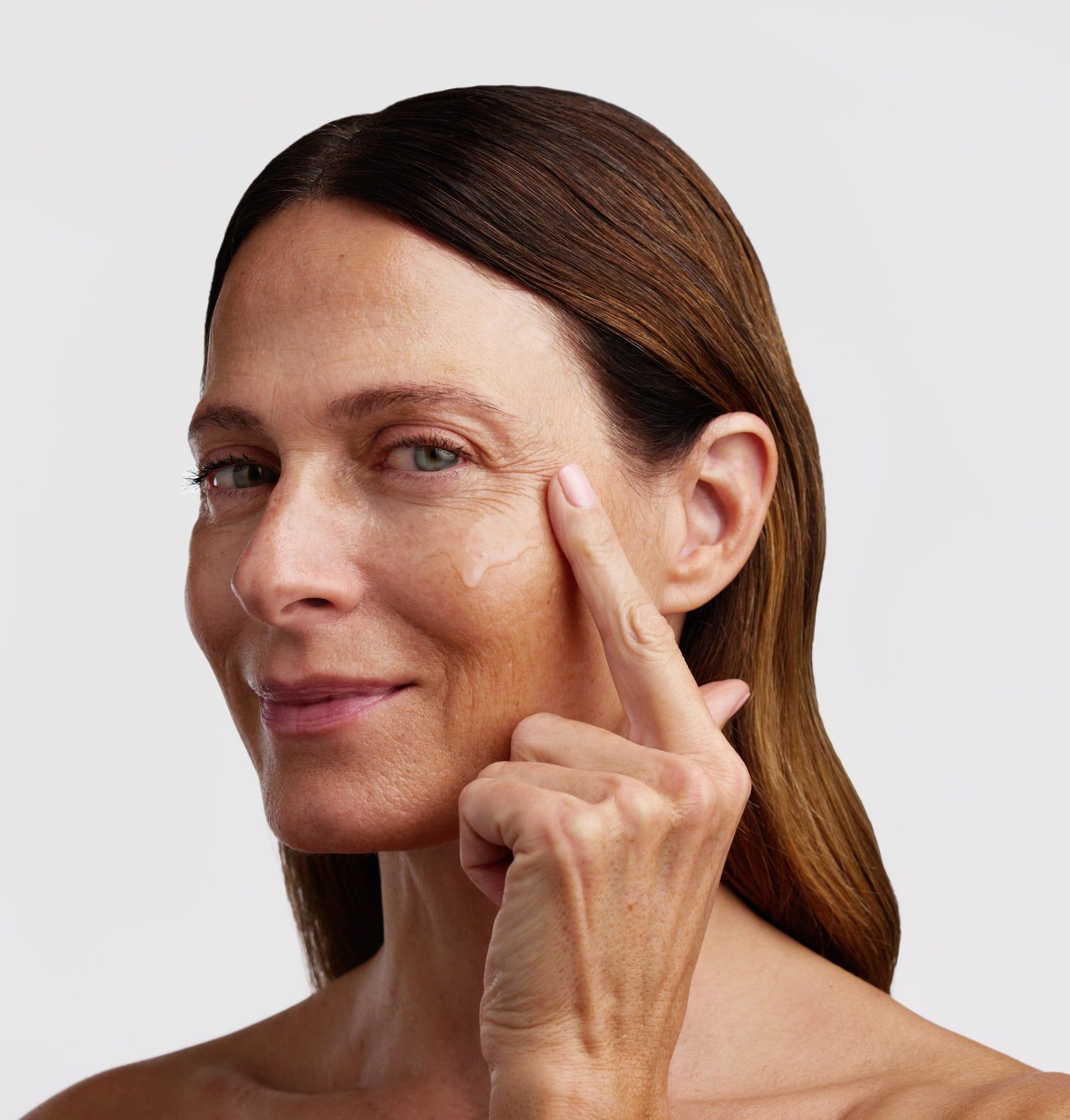 Frau berührt sanft ihre Gesichtshaut. Auf der Haut ist eine transparente Flüssigkeit sichtbar.