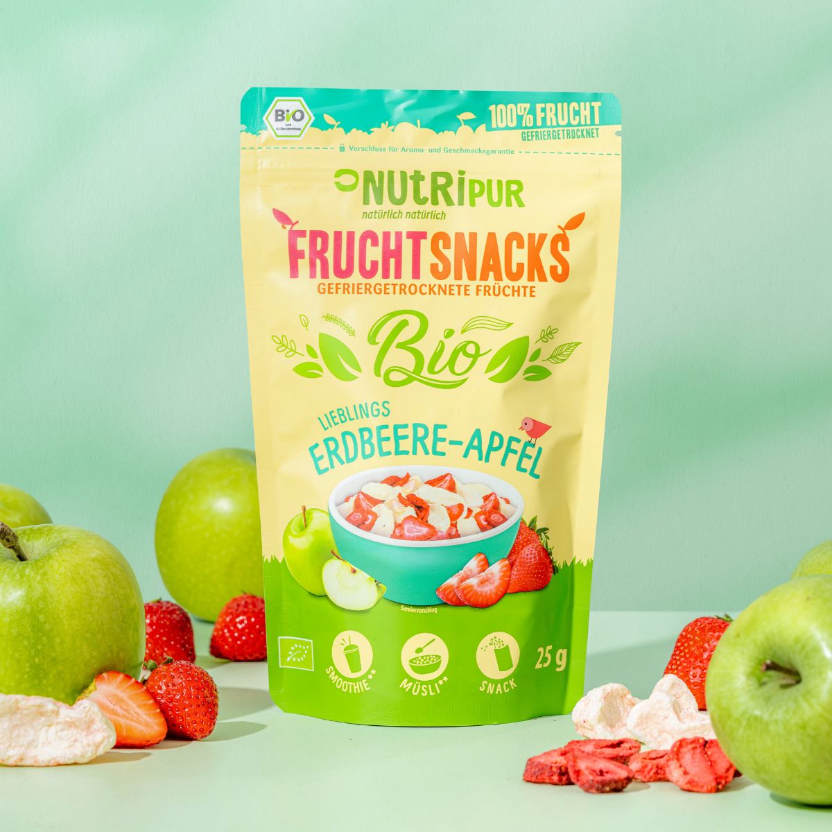 Beutel mit gefriergetrockneten Früchten. Äpfel und Erdbeeren umgeben den Beutel. Aufschrift: Frucht Snacks, Erdbeere-Apfel Bio.