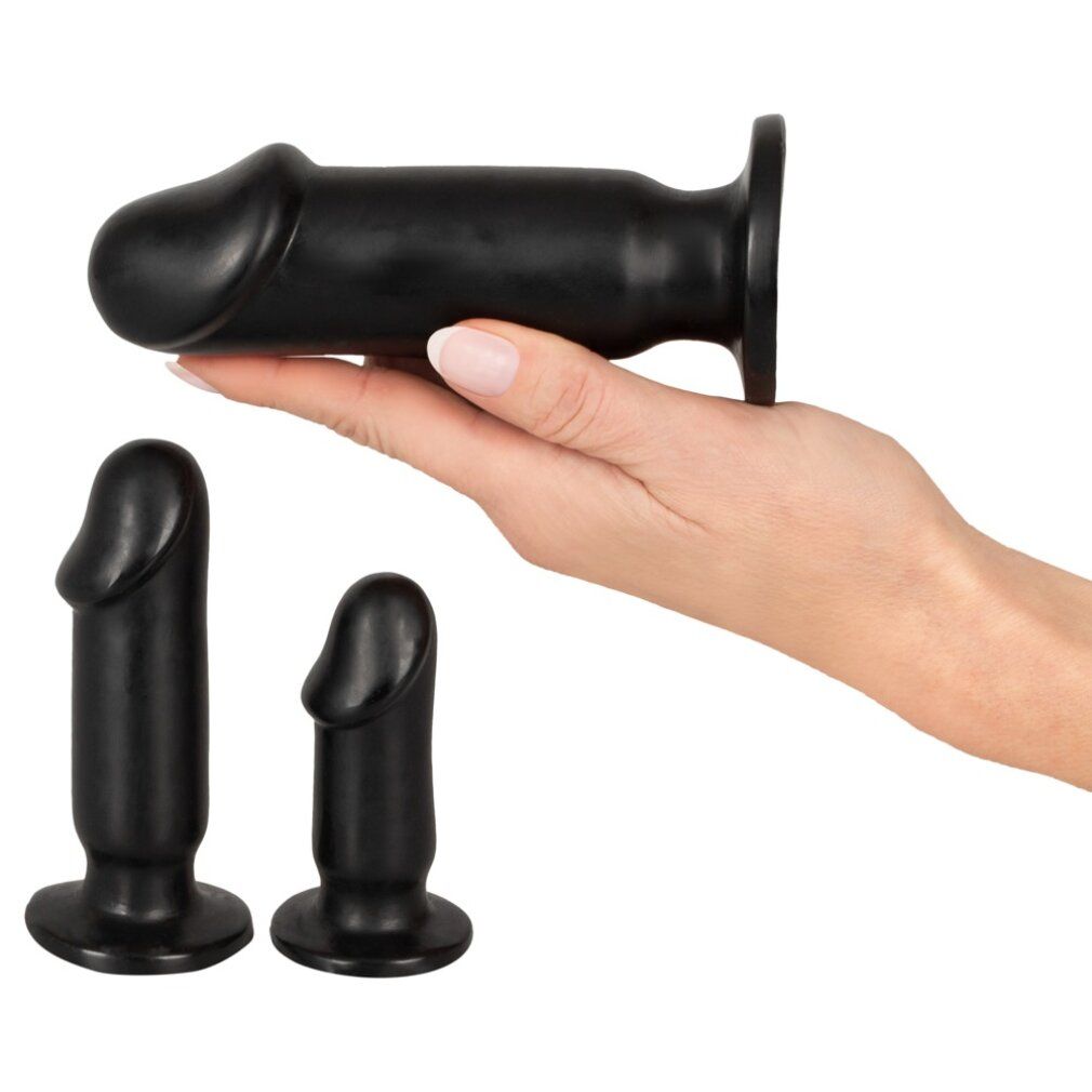 Drei schwarze Analplugs. Ein Plug wird von einer Hand gehalten. Die anderen zwei liegen daneben. Zylindrische Form mit abgerundeter Spitze.