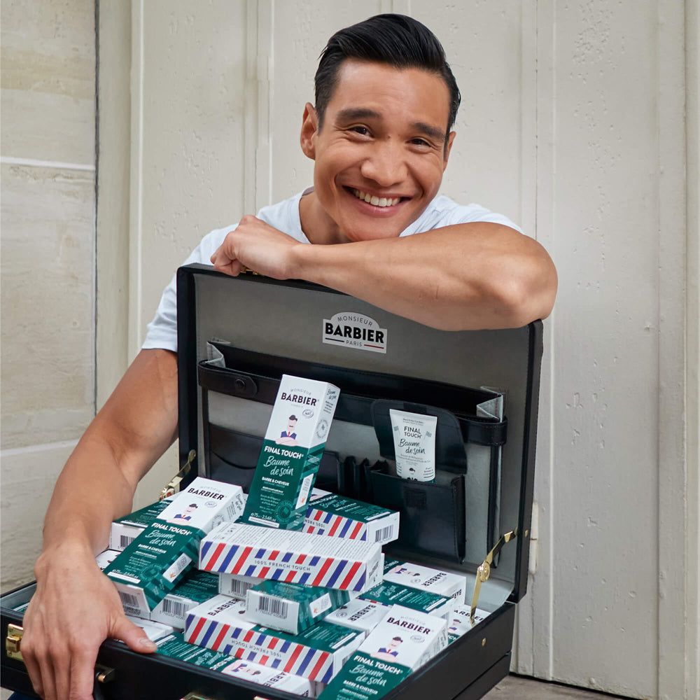 Mann mit Koffer voller Produkte. Koffer geöffnet, gefüllt mit Tuben und Schachteln. Aufschrift "BARBIER".