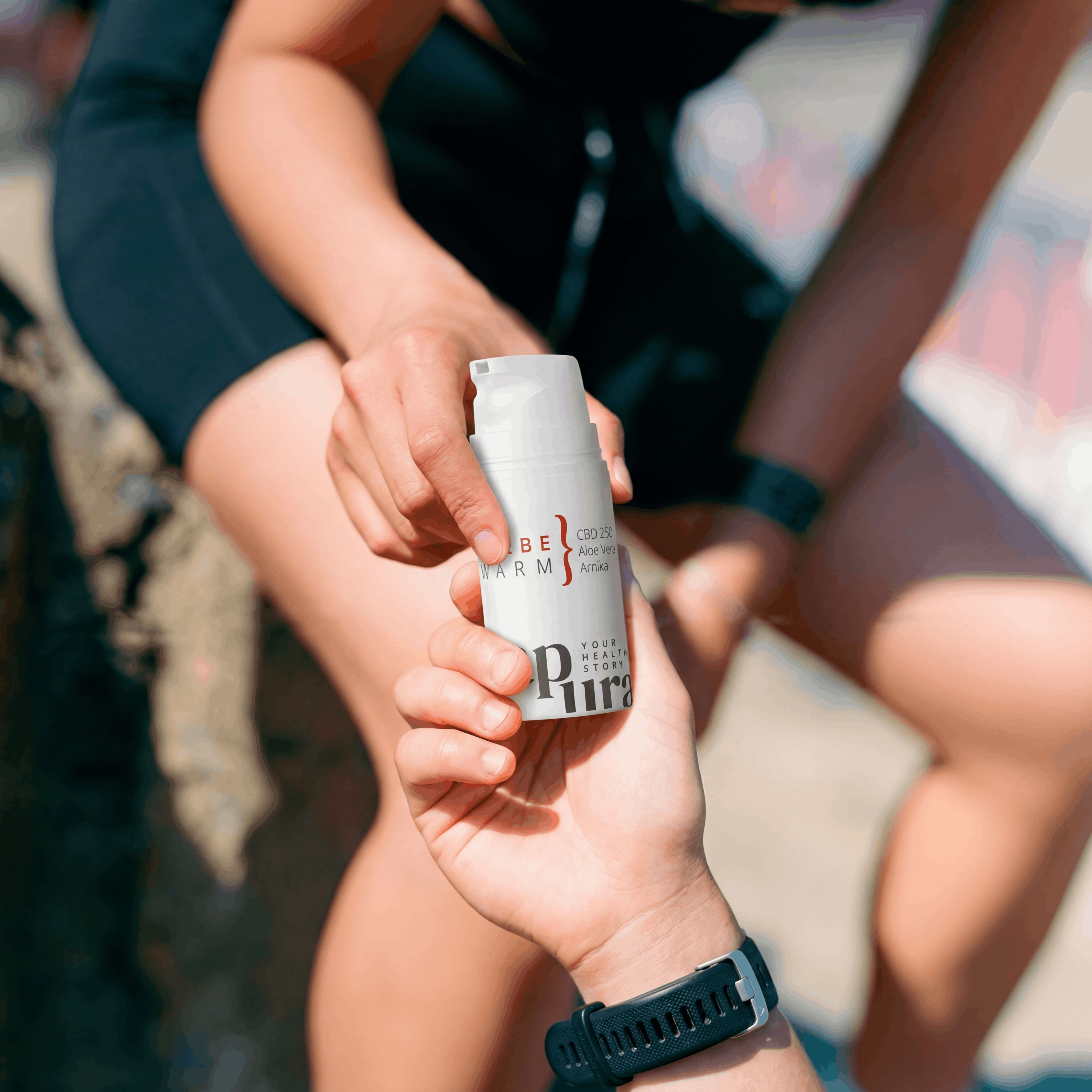 Zwei Hände reichen sich eine weiße Pumpflasche mit "CBD SALBE WARM" und "CBD 250mg Aloe Vera Arnika".
