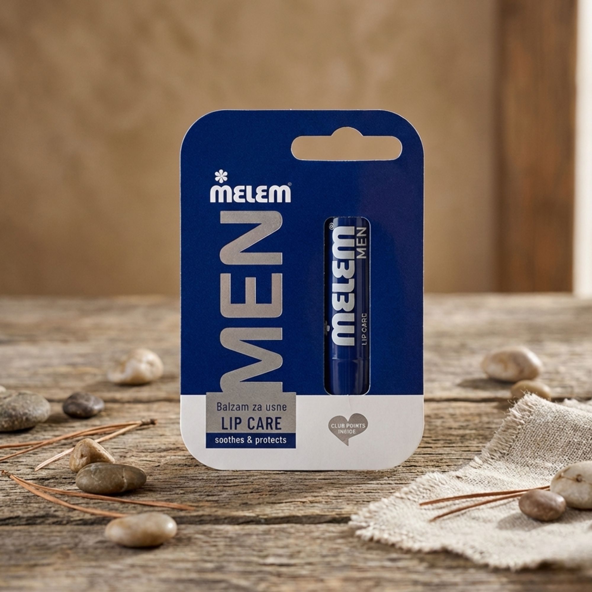 Blauer Lippenbalsam in Verpackung. Aufschrift: MELEM MEN, LIP CARE. Auf Holzuntergrund mit Steinen und Leinen.