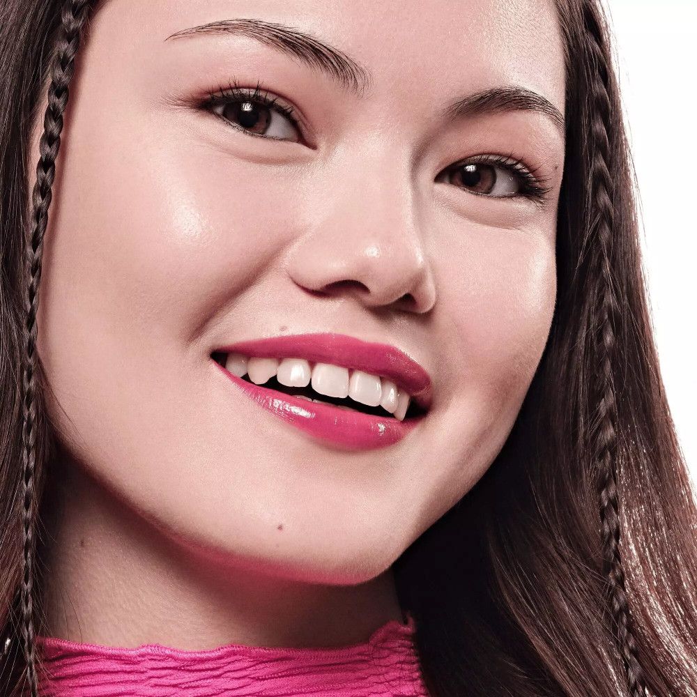 Porträt einer Frau mit pink getönten Lippen. Sie lächelt. Lange, geflochtene Haare.