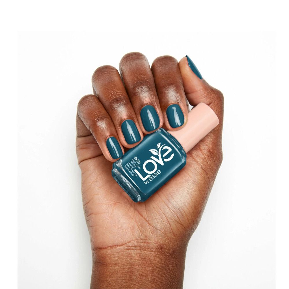 Hand mit lackierten Nägeln und Nagellackflasche. Flasche mit Aufschrift 'Love by essie'.