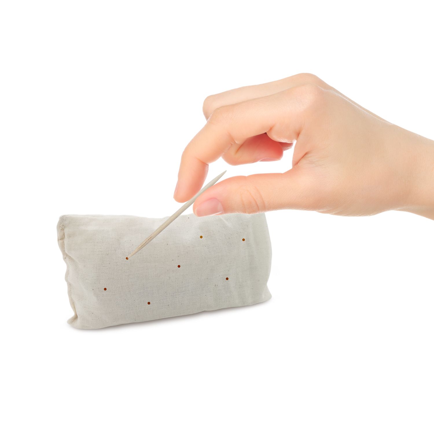 Hand hält Holzstäbchen über Stoffkissen. Kissen beige, rechteckig. Stäbchen wird in Kissen gesteckt.